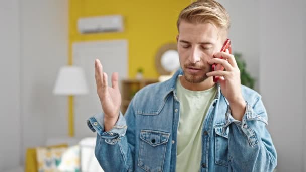 自宅で深刻な表現でスマートフォンで話している若い白人男性 — ストック動画