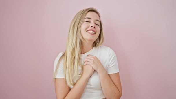 孤立したピンクの背景の上にハートで自信を持って微笑む若い金髪の女性 — ストック動画
