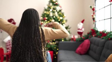 Afrikalı bir kadın Noel ağacının yanında arkada oturuyor.