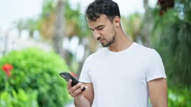 Genç İspanyol adam parkta akıllı telefon kullanıyor.