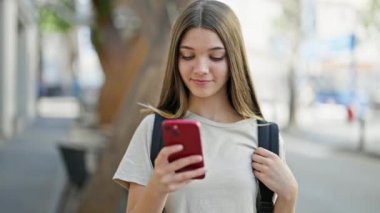 Sırt çantası takan genç ve güzel bir kız sokakta akıllı telefon kullanıyor.