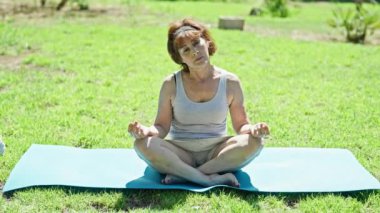 Orta yaşlı kadın parkta oturmuş yoga eğitimi alıyor.