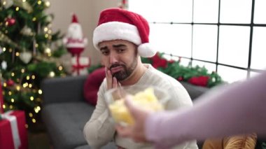 Kafası ve midesi ağrıyan İspanyol genç adam Noel ağacının yanında oturuyor.