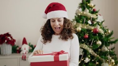Orta yaşlı İspanyol kadın Noel ağacının yanında hediyesini açıyor.