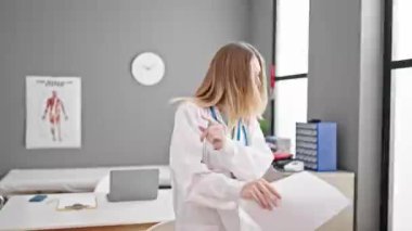 Genç sarışın doktor gülümseyerek klinikte dans ediyor.