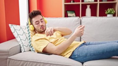 Young hispanic man listening to music sleeping on sofa at home