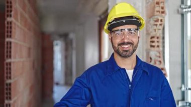 İnşaat alanında gülümseyen kasklı genç İspanyol işçi.