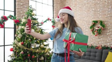 Genç ve güzel İspanyol kadın, akıllı telefonuyla Noel 'i evde kutlarken selfie çekiyor.