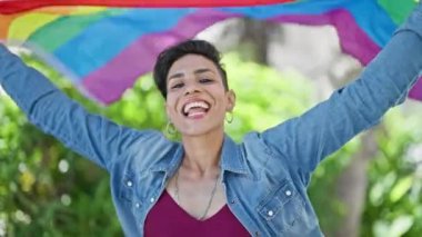 Parkta gökkuşağı bayrağı tutan güzel İspanyol kadın gülümsüyor.