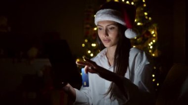 Tablet ve kredi kartıyla alışveriş yapan genç, güzel İspanyol kadın Noel 'i evde kutluyor.