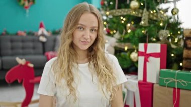Genç sarışın kadın Noel 'i kutluyor. Evde kalp hareketi yapıyor.