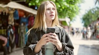 Sokak pazarında akıllı telefon kullanan genç sarışın kadın.