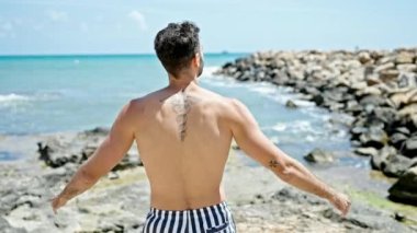 Genç İspanyol turist mayo giyip plajda kolları açık olarak dikiliyor.