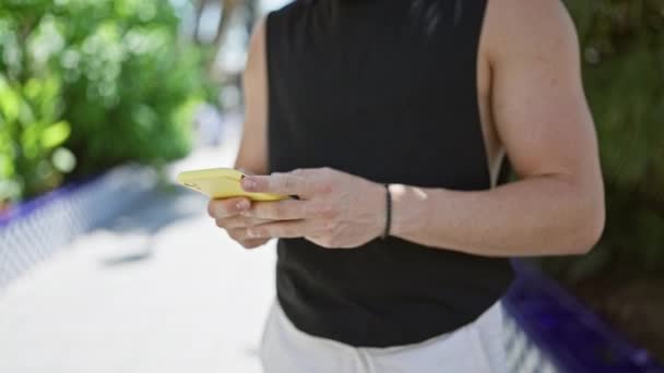 Молодий Іспаномовний Чоловік Носить Сонцезахисні Окуляри Використовуючи Смартфон Посміхаючись Парку — стокове відео