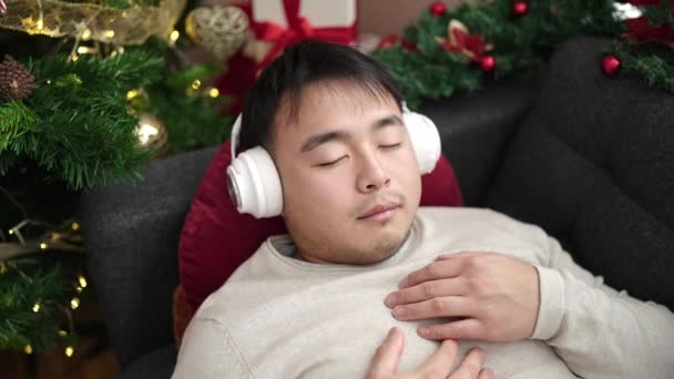 Joven Chino Escuchando Música Durmiendo Sofá Junto Árbol Navidad Casa — Vídeo de stock