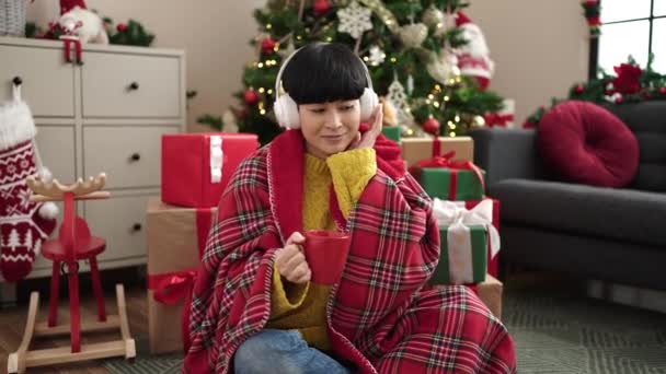 在家里听音乐的年轻中国女人在圣诞树旁喝咖啡 — 图库视频影像