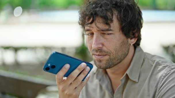 Jovem Hispânico Enviando Mensagem Voz Com Smartphone Sentado Banco Parque — Vídeo de Stock