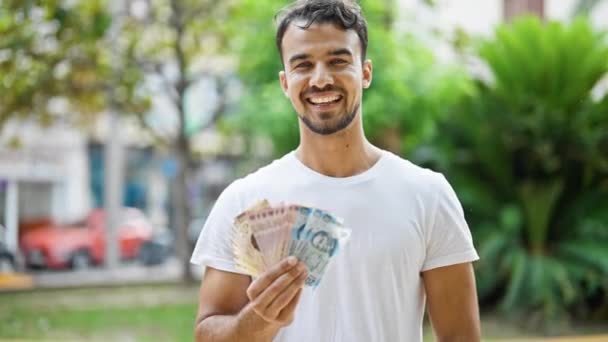 Joven Hispano Sonriendo Confiado Sosteniendo Pesos Mexicanos Parque — Vídeos de Stock