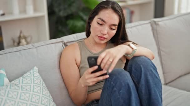 自宅でソファーで強調されたスマートフォンを使用して若い美しいヒスパニック女性 — ストック動画