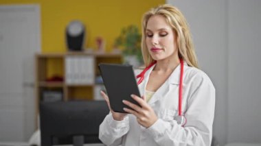 Klinikte dokunmatik ped kullanarak gülümseyen genç sarışın kadın doktor.