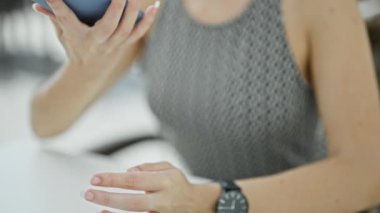 Genç sarışın kadın kahve dükkanının terasında oturmuş akıllı telefondan konuşuyor.