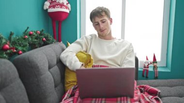Genç beyaz adam dizüstü bilgisayarda video seyrediyor evde Noel 'i kutluyor.