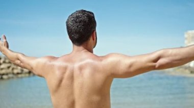Genç İspanyol turist plajda kollarını açmış üstsüz duruyor.