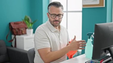 Gri saçlı iş adamı ofiste masa ve bilgisayar temizliyor.