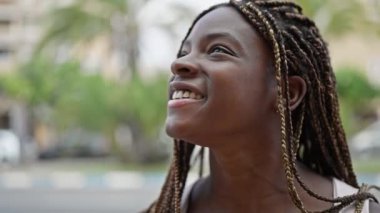 Afro-Amerikalı kadın gülümsüyor. Sokakta nefes alıyor.