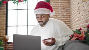 Afrikalı Amerikalı adam evde Noel 'i laptop ve kredi kartıyla kutluyor.