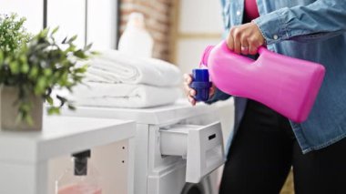 Young beautiful hispanic woman pouring detergent on washing machine at laundry room