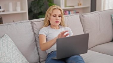 Genç sarışın kadın işini bitirip evdeki kanepede uzanmış televizyon seyrediyor.