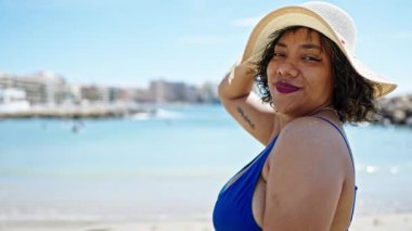 Genç ve güzel Latin kadın turist gülümsüyor. Mayolu ve plajda yaz şapkası takıyor.