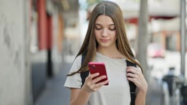 Sırt çantası takan genç ve güzel bir kız sokakta akıllı telefon kullanıyor.