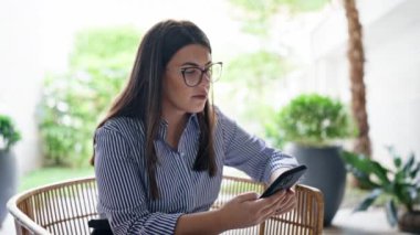 Ofis bahçesindeki sandalyede oturan akıllı telefon kullanarak gülümseyen genç ve güzel İspanyol kadın.