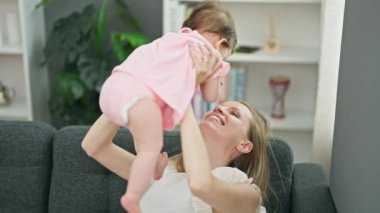 Anne ve kızı evde gülümseyerek bebeği kucağında tutuyorlar.