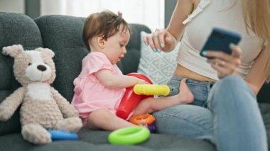 Anne ve kızı evde çember oynarken akıllı telefon kullanıyorlar.