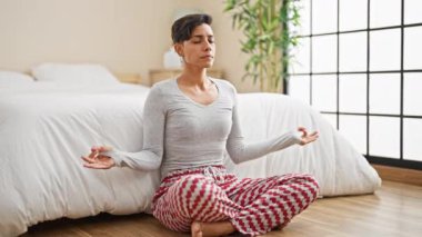 Genç ve güzel İspanyol kadın yoga yapıyor. Yatak odasında yerde oturuyor.