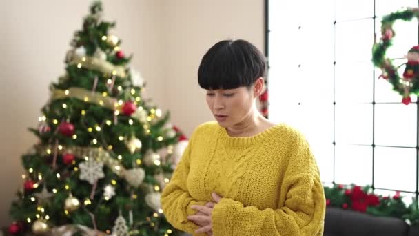 若いです中国人女性苦しみのために胃のために立ってクリスマスツリーに家 — ストック動画