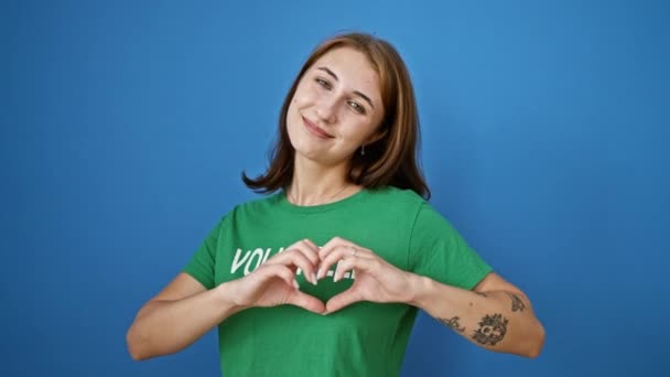Молода Жінка Доброволець Робить Жест Серця Посміхаючись Над Ізольованим Синім — стокове відео