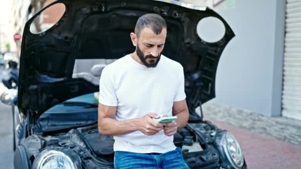 若いヒスパニック男性は 通りの車の故障のためにスマートフォンで保険でテキスト — ストック動画