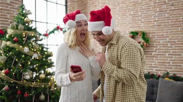 Man and woman couple celebrating christmas using smartphone hugging each other at home