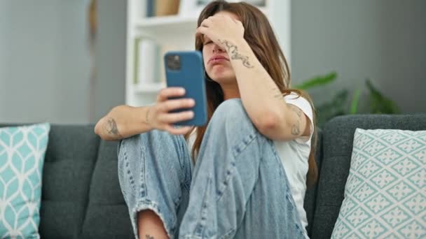 自宅で泣いているスマートフォンを使用してソファに座っている若い美しいヒスパニックの女性 — ストック動画