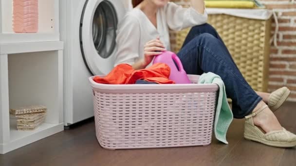 洗濯室で笑顔で洗濯機に傾いている若い赤毛の女性 — ストック動画