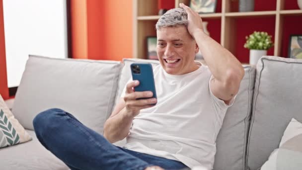 年轻的高加索人生气地坐在家里的沙发上 用智能手机 — 图库视频影像