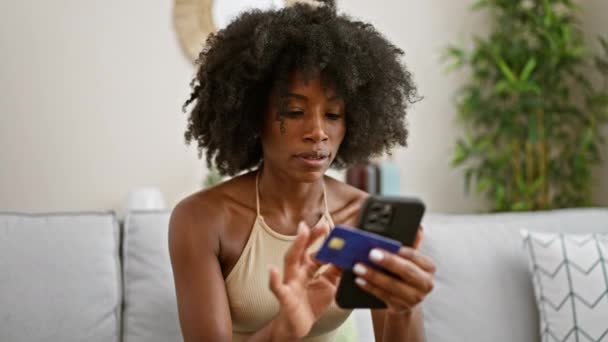 アフリカ系アメリカ人女性のショッピングでスマートフォンやクレジットカードを自宅でソファに座って — ストック動画