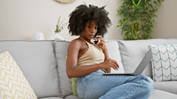 アフリカ系アメリカ人女性 自宅でラップトップの読書用紙を使用してスマートフォンで話す — ストック動画
