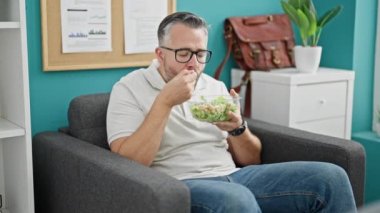 Gri saçlı iş adamı ofiste salata yiyor.