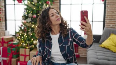 Orta yaşlı İspanyol kadın evde Noel 'i kutlarken selfie çekiyor.