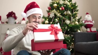 Evde Noel ağacının yanında oturan İspanyol bir adam hediye paketini açıyor.